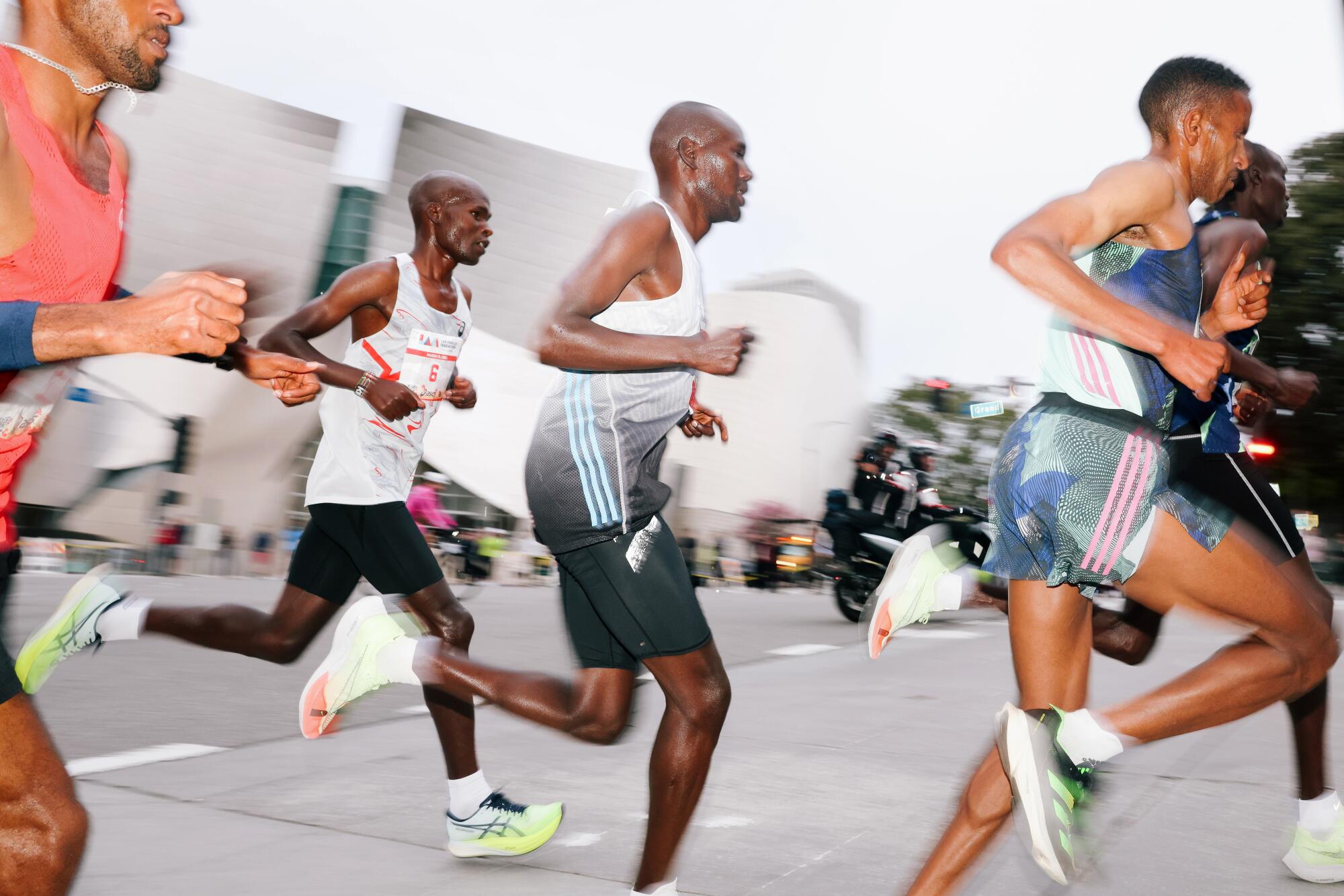 Five men run on a street. Their skin glistens with sweat.